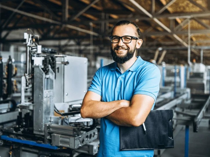 A smiling engineer with arms crossed on a factory floor